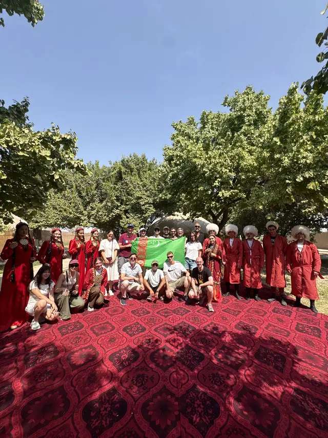 A tour group with the flag of Turkmenistan and folk dancers in national dress